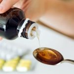 Young woman taking medicine on spoon at home.
