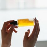 Hands of cropped white woman holding cosmetic serum bottle with pipette near window. Texture of serum